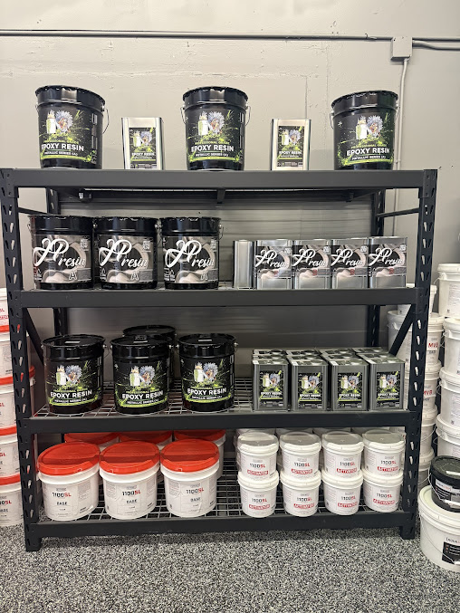A black steel shelf stacked with epoxy kits, pigment tubs and buckets in the shop