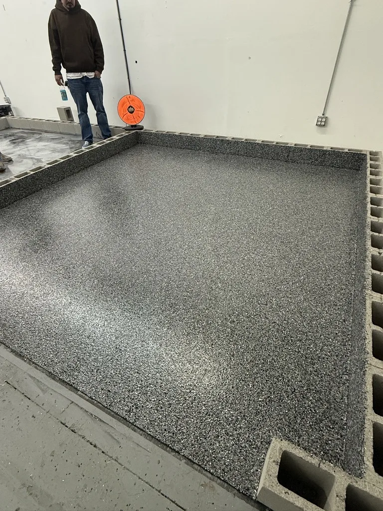 A person broadcasting flake over a wet base coat on a small slab, the flake field spreading toward the camera