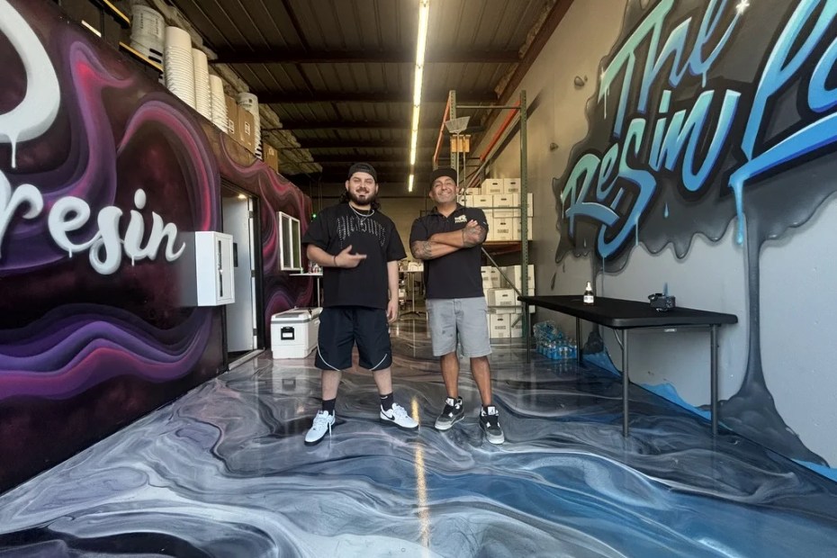 Exclusive Resin Supply and The Resin Lab owners standing on a metallic floor between the JP Resin and Resin Lab murals in Tracy, CA