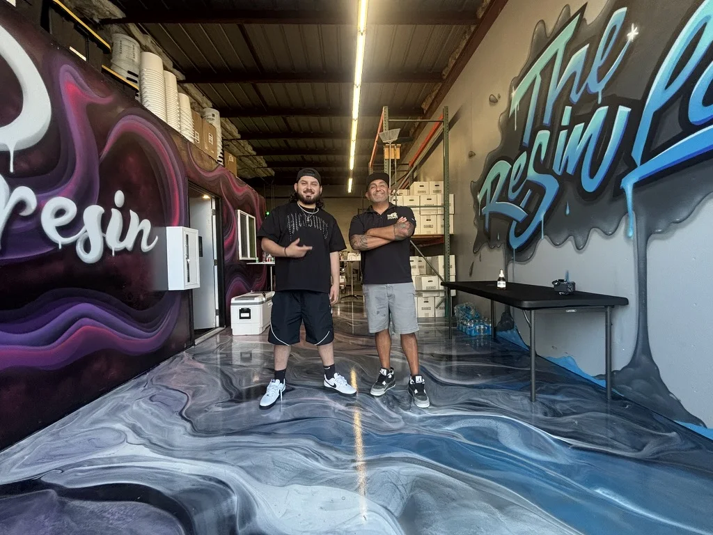 Exclusive Resin Supply and The Resin Lab owners standing on a metallic floor between the JP Resin and Resin Lab murals in Tracy, CA